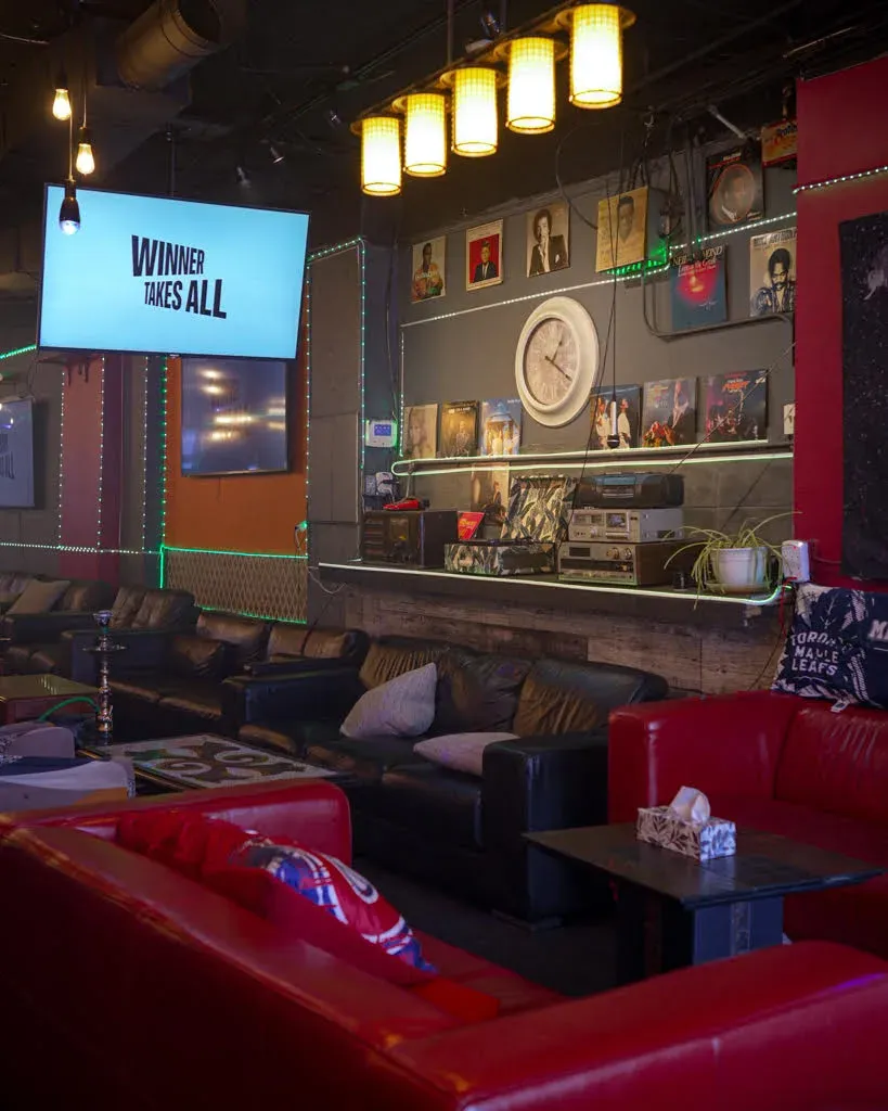 Leather couches under the vinyl record wall at Dose Shisha, with a screen above and Leafs and Canadiens cushions